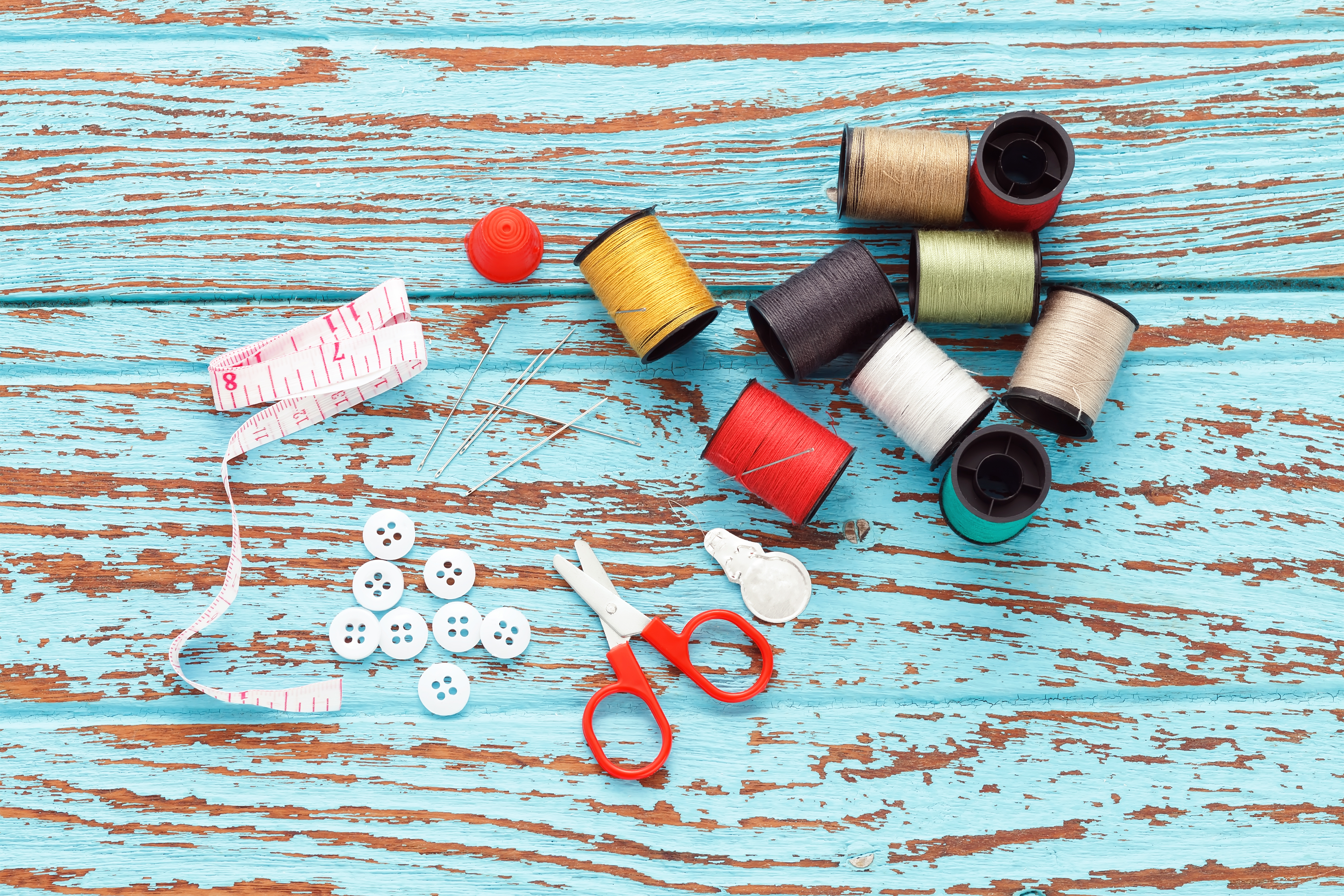 Sewing thread, scissors, measure, and buttons on a wooden blue table