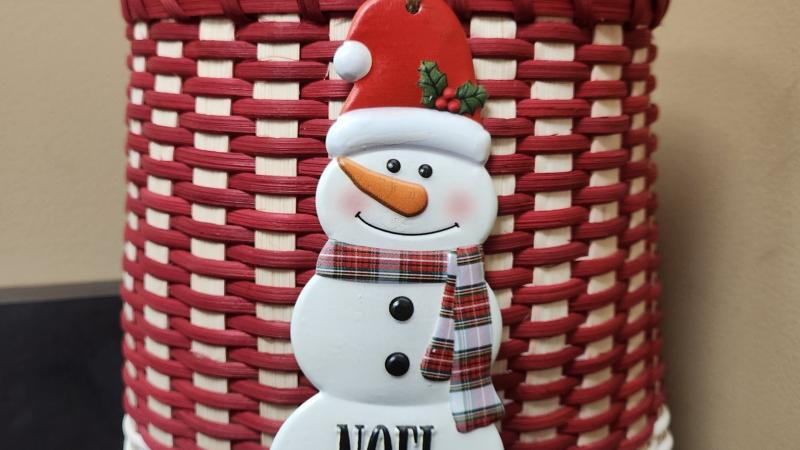 A Red and White Christmas basket with a snowman on the front and the word NOEL on the bottom of the snowman.