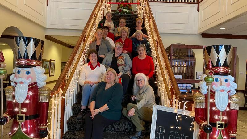 A picture of the loyal homemakers sitting on a staircase decorated for Christmas.